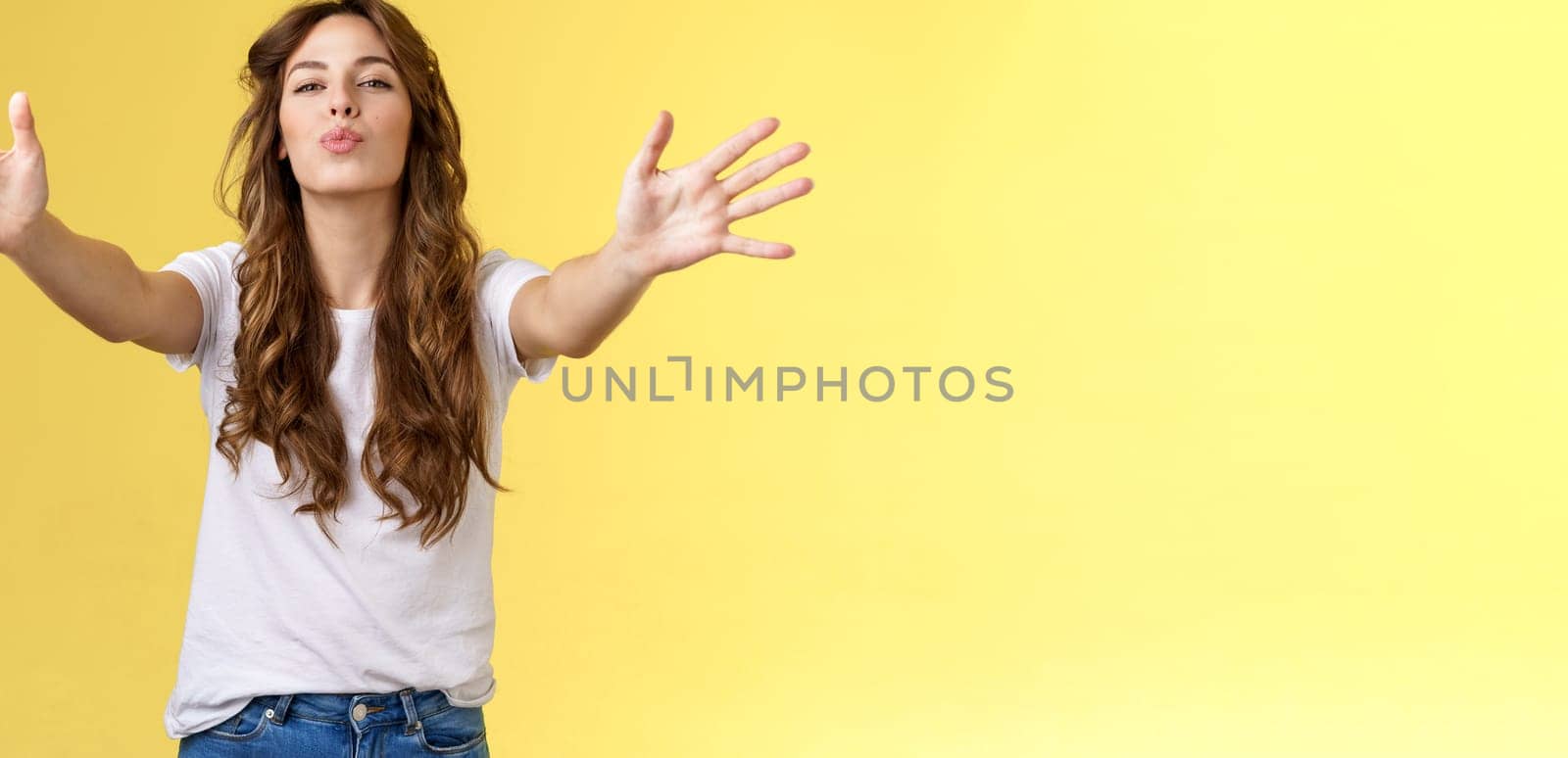 Wanna kiss you. Friendly passionate attractive urban girl casual outfit reach camera extend arms cuddles hugging folding lips send air muah romantic tempting attitude give hug yellow background.