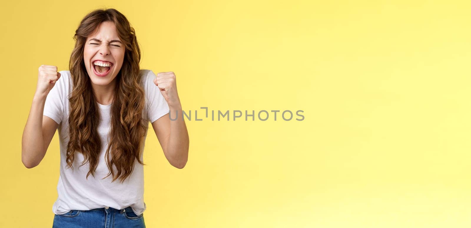 Cheerful excited happy enthusiastic girl yelling rooting wanna win badly fist pump celebratory satisfied awesome success winning triumphing joyfully close eyes shaking clench arms yellow background. Lifestyle.