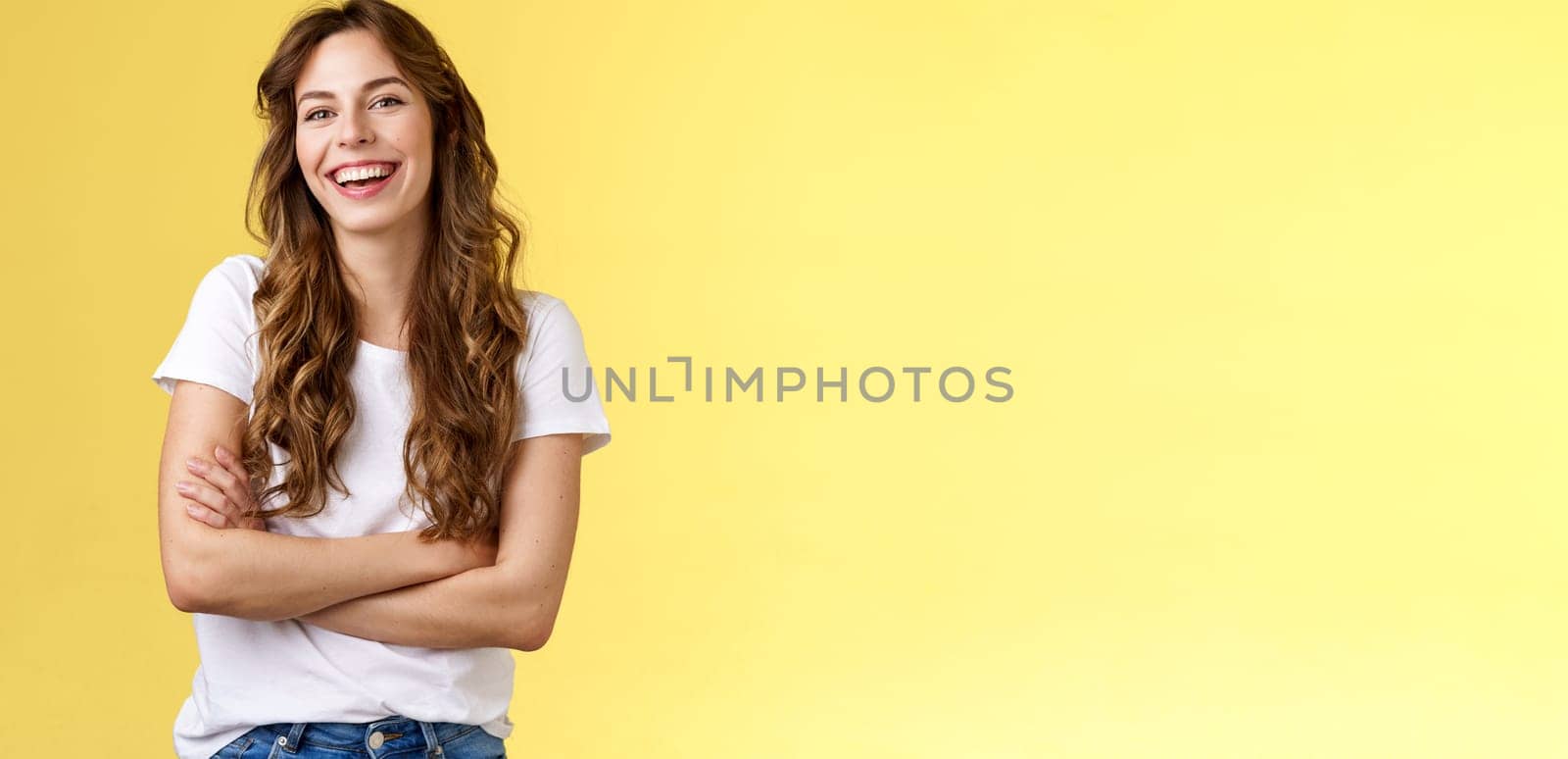 Entertain me. Friendly charismatic female long curly haircut laughing joyfully hang out friends cross arms chest feel chilly slightly cold have amusing pleasant conversation yellow background.