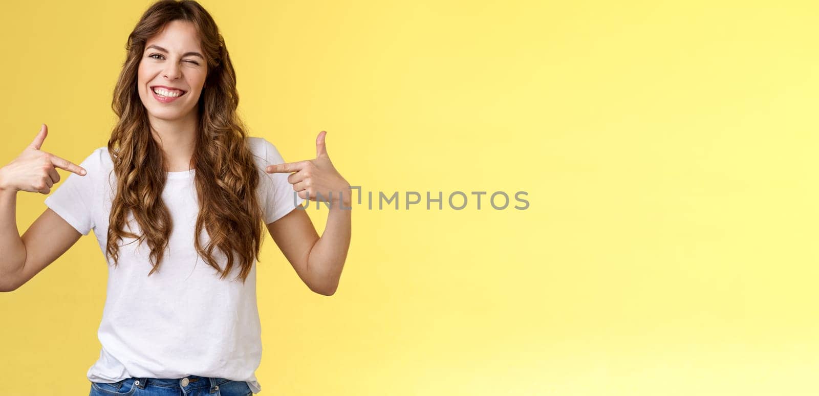 You would not regret this. Sassy good-looking outgoing daring young woman pointing center copy space indicating herself winking joyfully show perfect candidature stand yellow background.