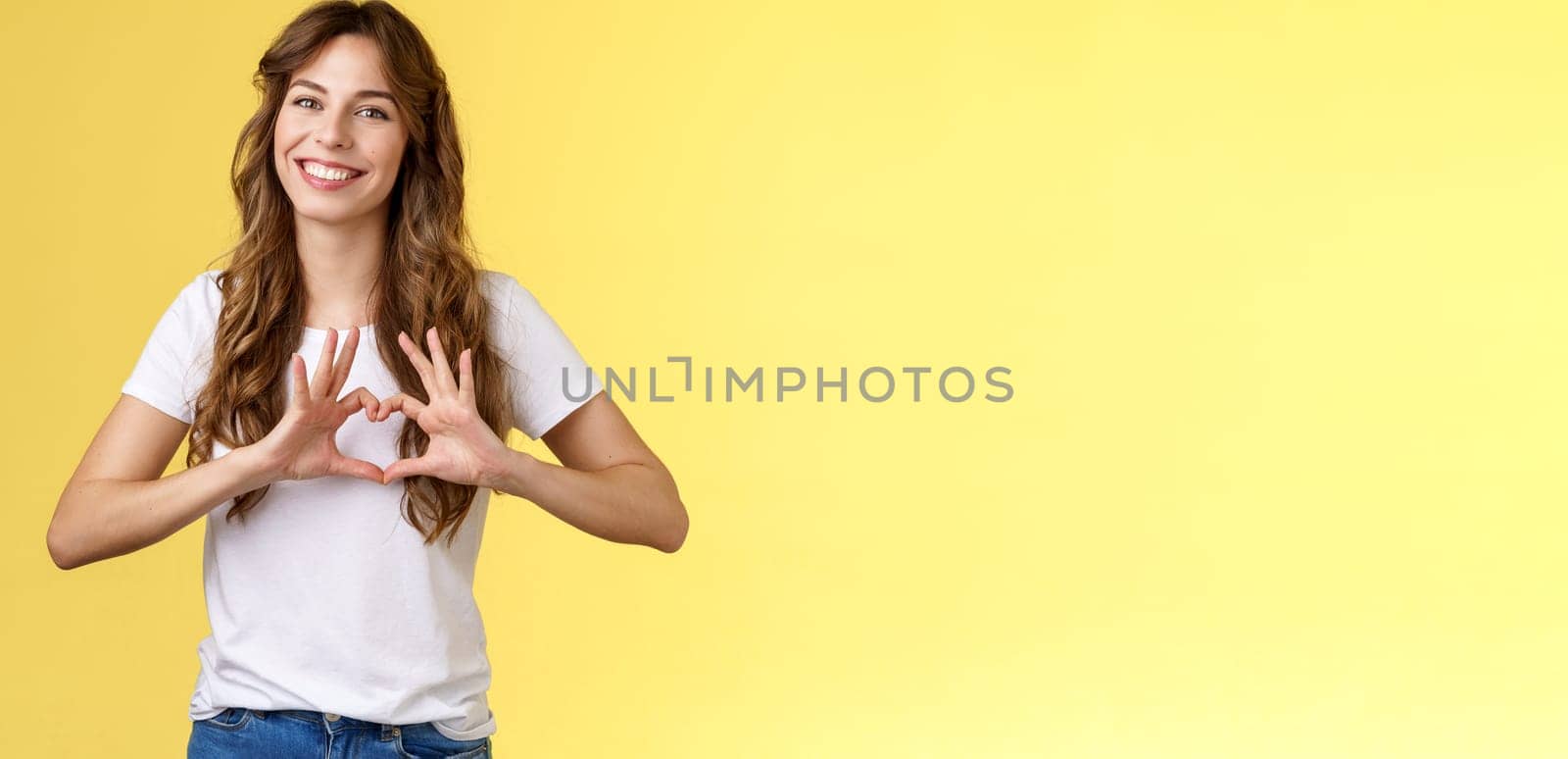 You my valantine. Tender confident adult girl curly hairstyle show heart gesture near chest express romantic sympathy feelings smiling delighted cherish relationship boyfriend yellow background by Benzoix