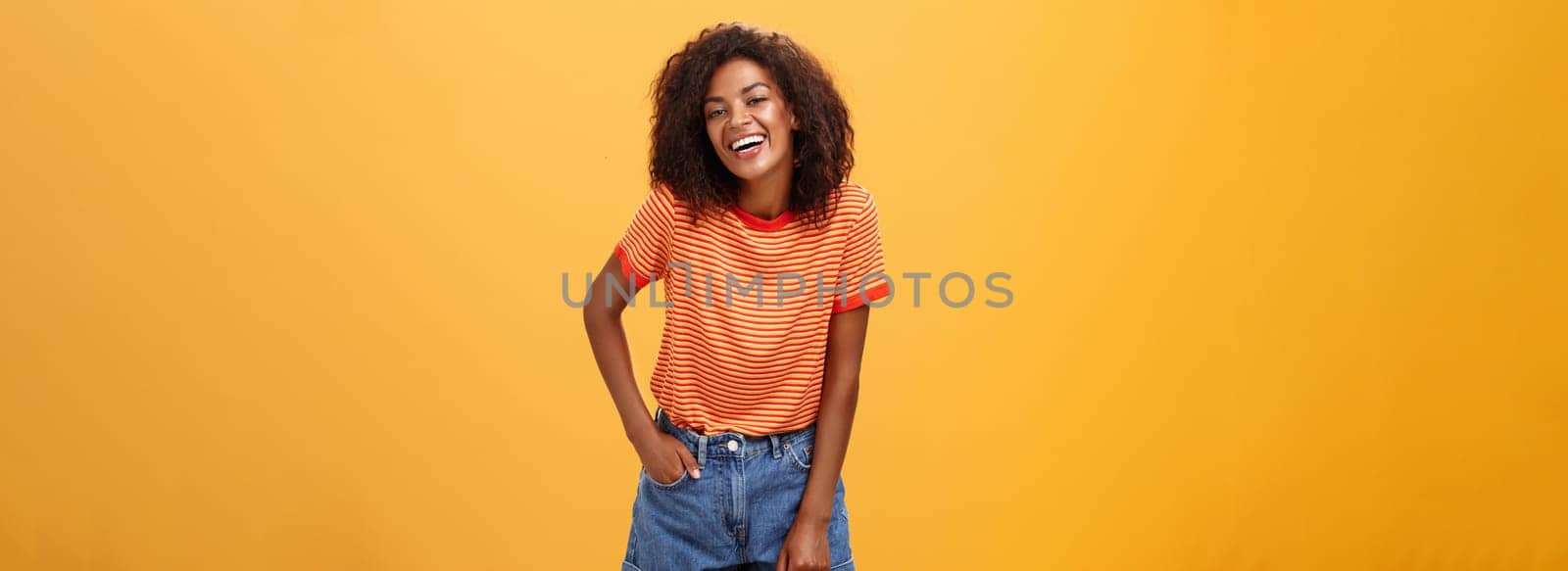 Portrait of charismatic charming african american stylish african american female in trendy shorts and t-shirt laughing happily enjoying talking with cool people laughing posing over orange background. Lifestyle.