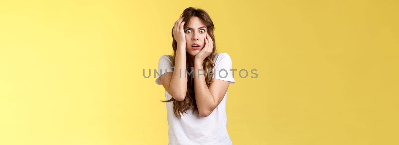 Oh my god someone save me. Scared stunned intense panicking young woman grab head stare camera frightened open mouth gasping shocked standing stupor yellow background timid insecure by Benzoix
