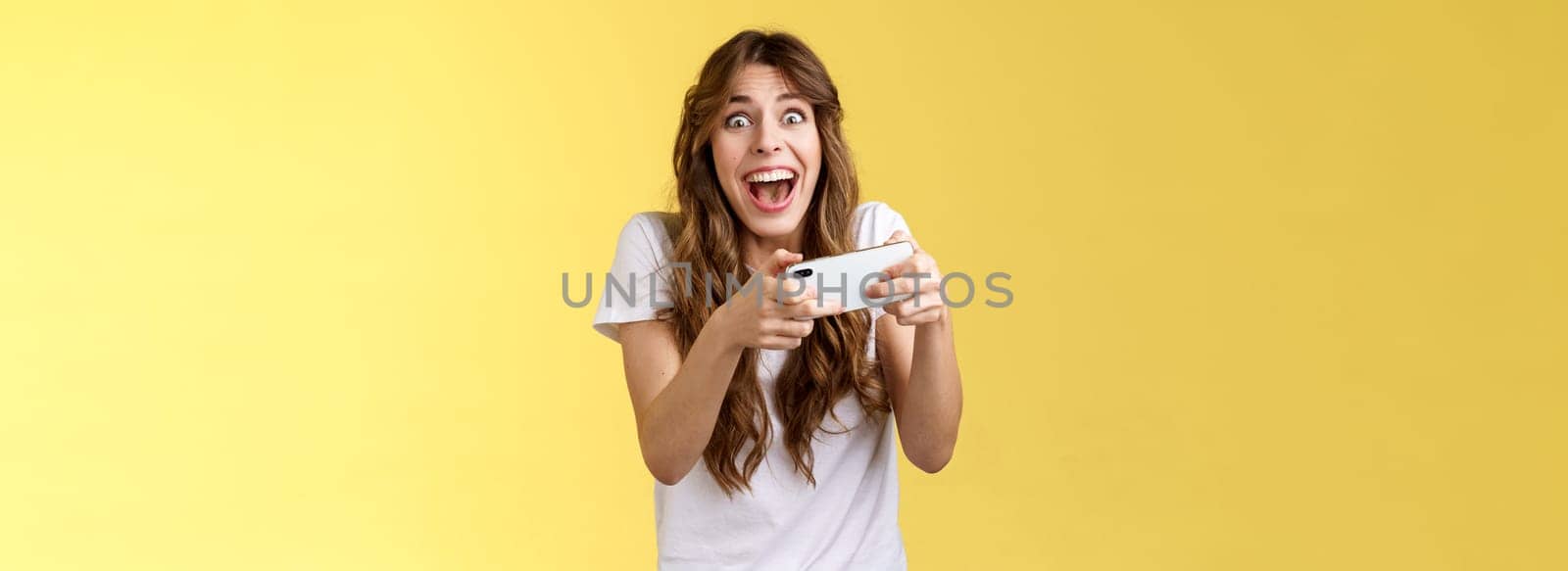 Extremely happy thrilled playful girl gamer playing awesome great new smartphone game hold mobile phone horizontal cheering look camera astonished impressed beating record yellow background by Benzoix