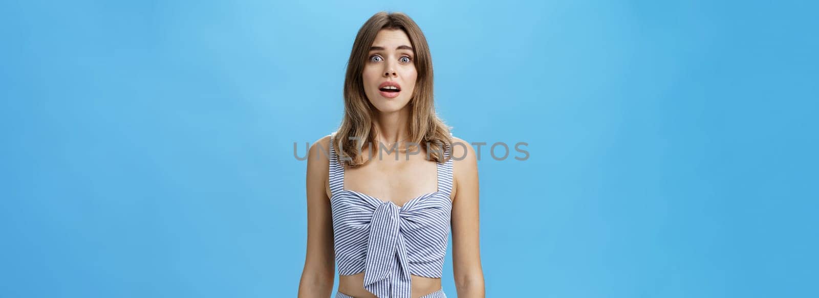 Portrait of silly desperate and upset cute attractive woman with diastema open mouth gasping and frowning from worry and troublesome situation looking with begging eyes at camera over blue wall. Emotions concept
