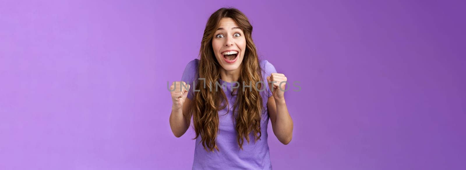 Cheerful hopeful cute female fan celebrating awesome news winning lottery yelling pleased happy smiling broadly fist pump joyfully happiness success triumph pose purple background.