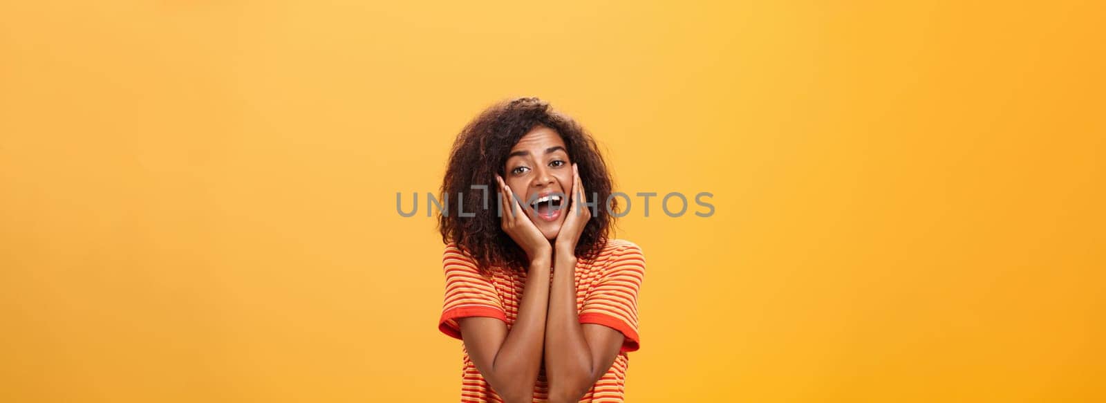 Dreamy good-looking stylish young african female with curly hairstyle sighing leaning head on palms gazing with affection and admiration at camera being in love imaging prince on white horse. Lifestyle.