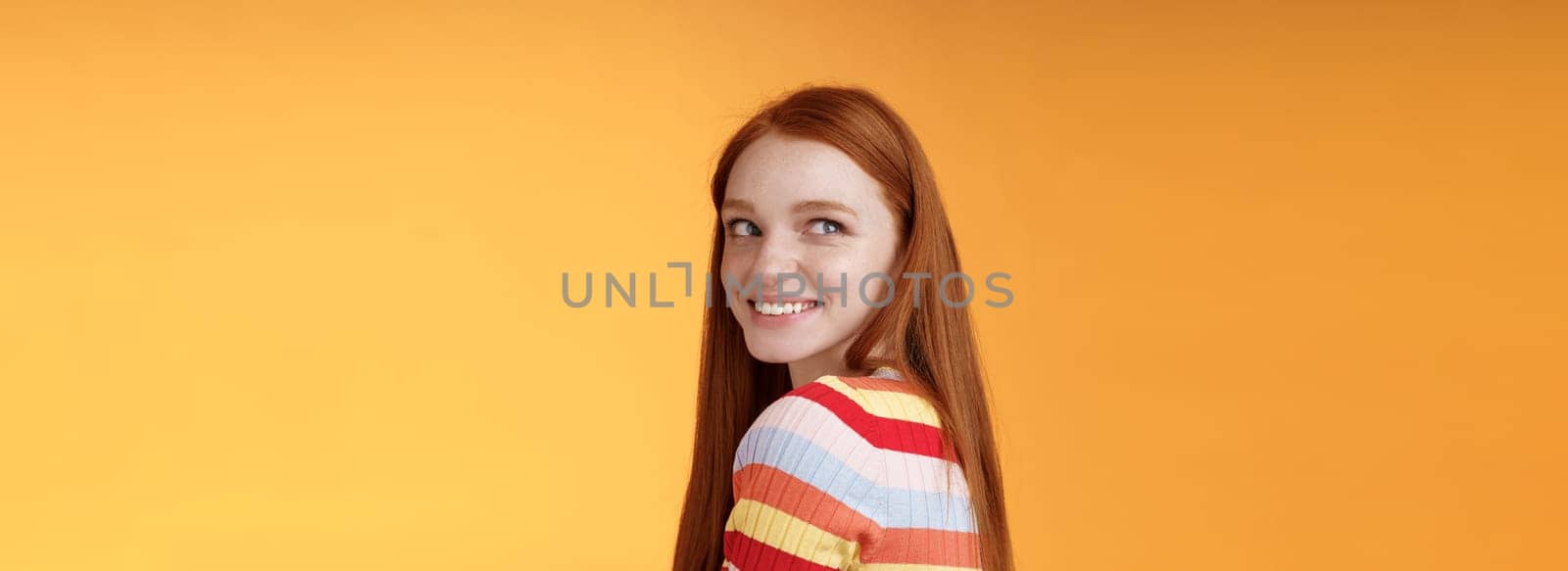Tender romantic carefree european redhead girlfriend turning behind look left amused smiling pleased coquettish gaze standing orange background flirty romantic mood wanna receive date invitation by Benzoix