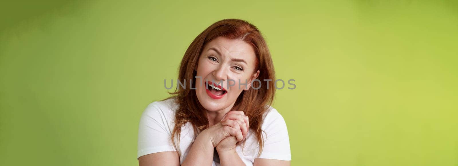 Close-yp touched tender kind redhead middle-aged granny sighing look admiration delight clasp hands heartwarming lovely scene smiling tilting head impressed satisfied stand green background by Benzoix