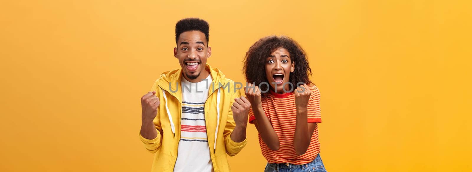 Two friends cheering and supporting mate on competition yelling joyfully clenching fists in supportive geture smiling broadly waiting with amazement and excitement for win and victory. Lifestyle.