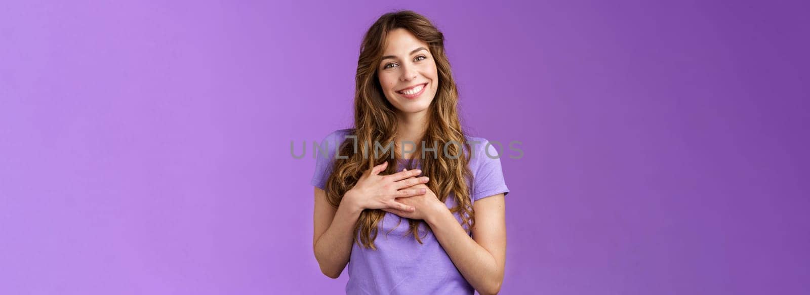 Tender charming grateful lovely curly-haired girl feel delighted sympathy touch heart cherish cute heartwarming date smiling broadly stand purple background joyful grateful appreciate effort.