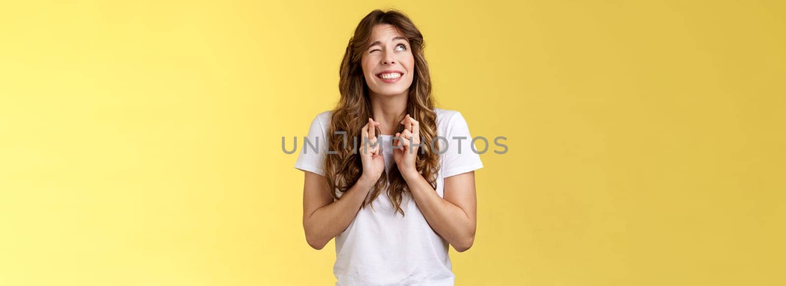 Hopeful optimistic enthusiastic girl believe god help smiling broadly close eyes make wish peeking up one eye smiling broadly cross fingers good luck implore Lord wish come true yellow background by Benzoix