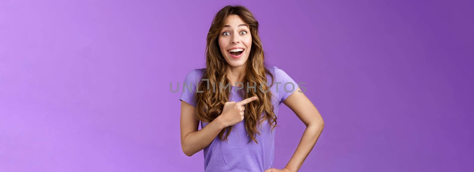 Lively excited enthuasitic good-looking woman curly hairstyle open mouth fascinated look admiration joy share awesome place location pointing left smiling broaldy thrilled purple background.