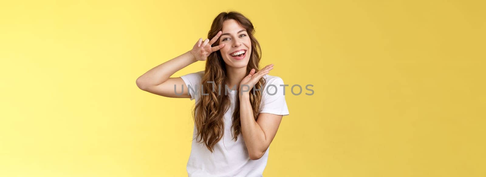 Lively enthusiastic attractive carefree woman enjoy relaxed weekends summer holiday have fun smiling broadly tilt head show peace victory sign joyfully introduce herself posing yellow background. Lifestyle.