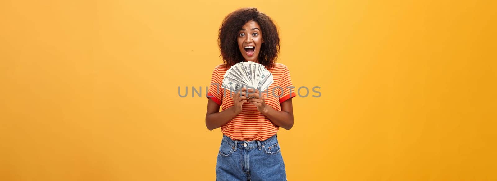 Woman cannot hide happiness winning lottery. Portrait of surprised and happy lucky african american young woman with curly hair holding bunch of money and yelling from delight receiving paycheck. Copy space