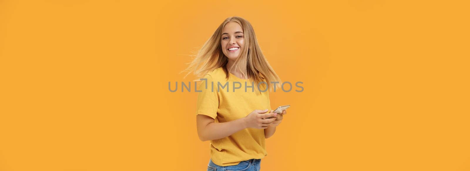 Girl feeling happy receiving message from him. Portrait of carefree charming woman with new haircut waving head standing half-turned, turning to camera with pleased cute smile holding smartphone. Emotions and technology concept