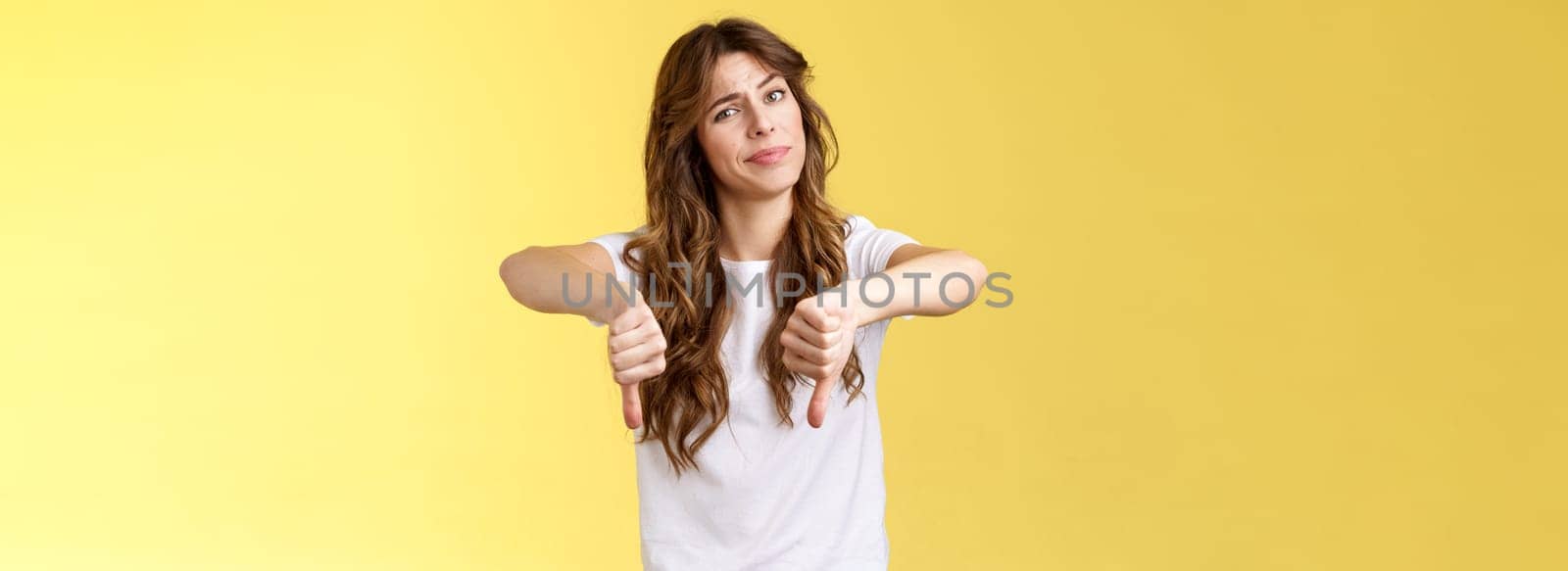 Honestly very bad. Disappointed upset curly-haired girl tilt head smirk displeased disagree show thumbs down sign dislike unimpressed awful idea stand yellow background uninterested.