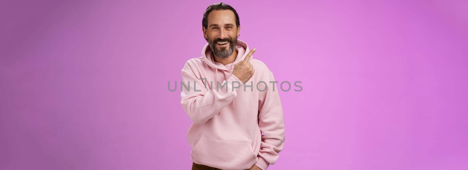 Charming friendly happy mature man 50s bearded grey hair laughing happily pointing upper left corner behind showing proudly family members standing purple background having fun stay positive. Lifestyle.