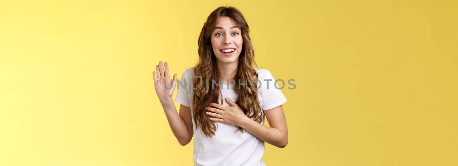 Girl introduce herself friendly joyful casual conversation smiling broadly hold hand heart raise palm waving swear tell truth be honest grinning make promise oath stand yellow background say hi. Lifestyle.