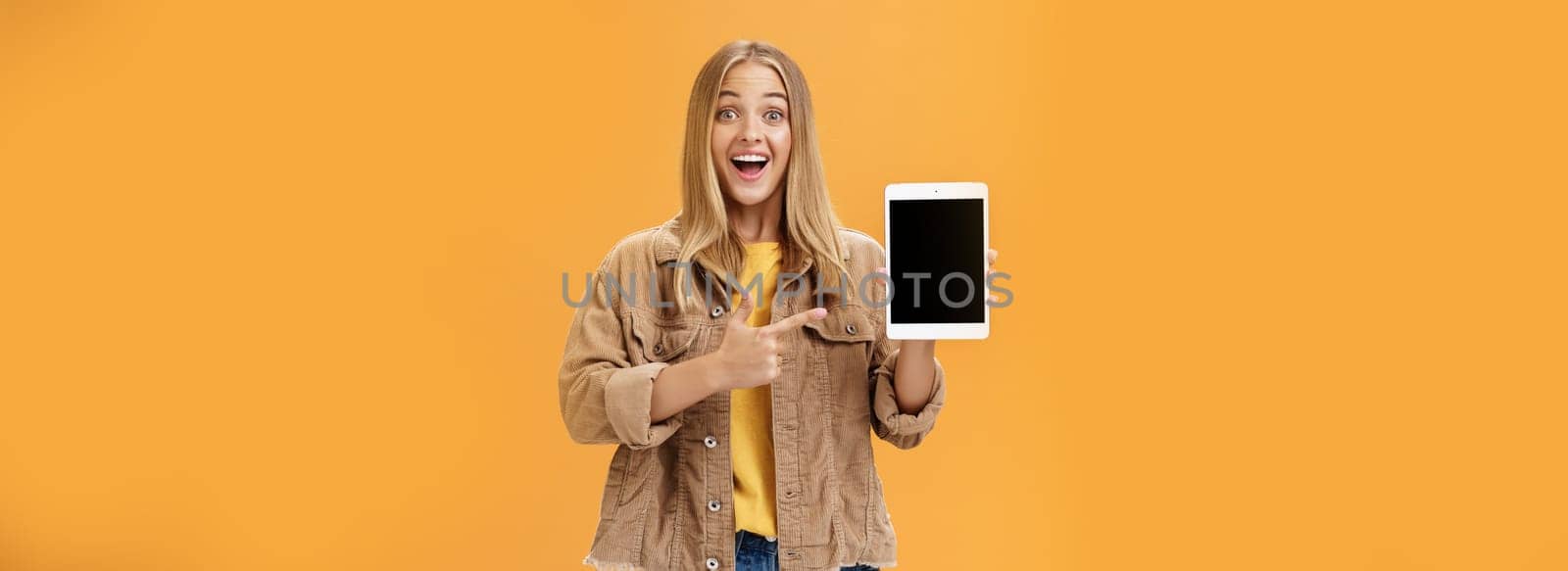 Woman showing friends new digital tablet first purchace of autumn. Charismatic and enthusiastic excited caucasian female with tanned skin and fair hair in corduroy jacket pointing at gadget screen. Emotions and technology concept