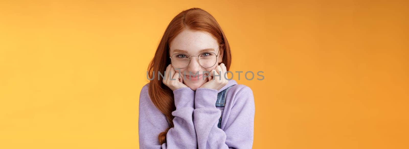 Lovely cute redhead sweet silly girl geek university student wearing glasses lean hand smiling tenderly look affection adore listen sensual confessions boyfriend, standing orange background.