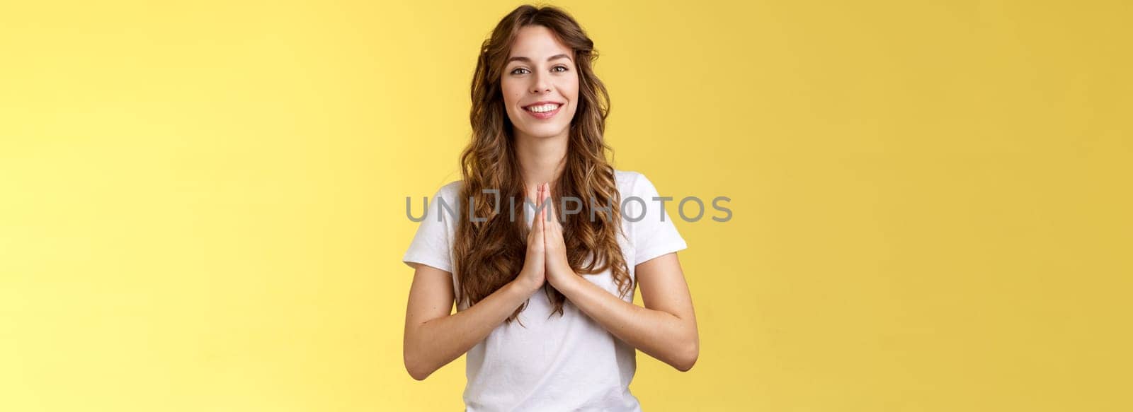 Cheerful confident outgoing young polite girl say namaste greeting asian guests smiling gladly thanking for visit hold hands pray supplication gesture asking favour begging stand yellow background by Benzoix