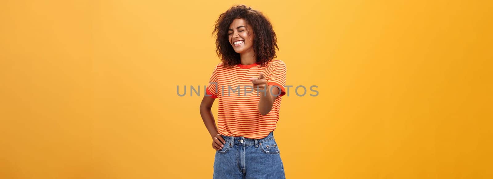 Girl pointing at funny and hilarious friend approving good joke. Amused and entertained attractive dark-skinned female with afro hairstyle laughing with closed eyes indicating at camera joyfully by Benzoix