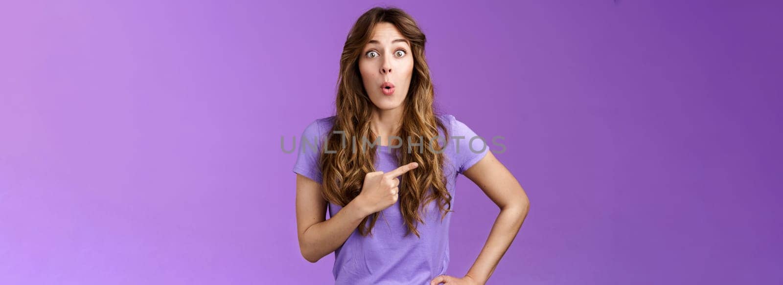 Impressed curious attractive young feminine girl introduce awesome place sharing info cool product fold lips look camera wondered astonished discuss awesome promo stand purple background.
