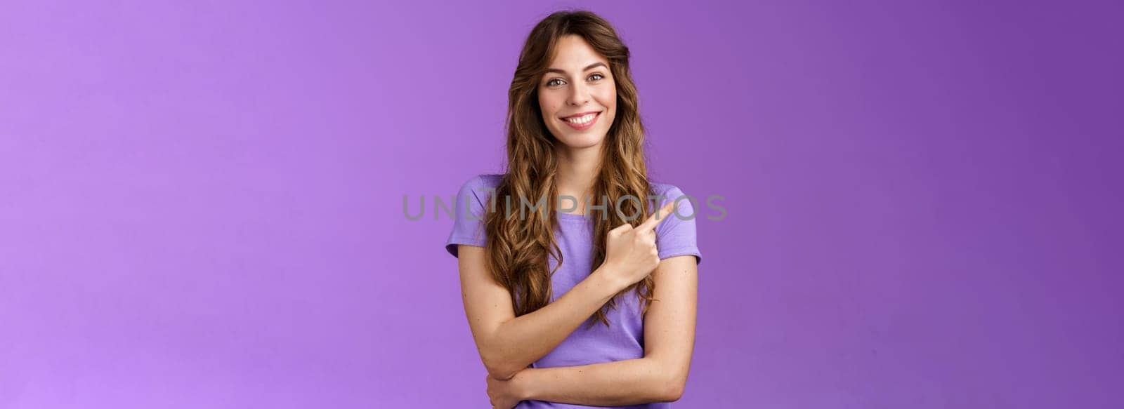 Cheerful smart confident assertive curly-haired caucasian female share link pointing index fingers upper left corner smiling broadly give advice what place visit stand purple background. Lifestyle.