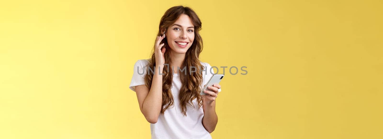 Stylish good-looking carefree urban girl put on earphones listen music wireless earbud touch headphone smiling delighted camera found awesome new track hold smartphone listen music by Benzoix