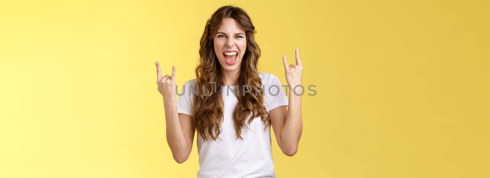 Going wild. Daring amused good-looking european curly-haired girl acting thrilled excited having fun enjoy awesome concert show yeah rock-n-roll heavy metal gesture grimacing satisfied.
