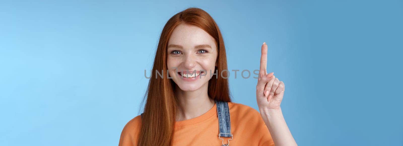 Confident happy charismatic ginger girl blue eyes freckles helpful showing product raising index finger up pointing cool copy space smiling broadly made choice recommend pick, studio background by Benzoix