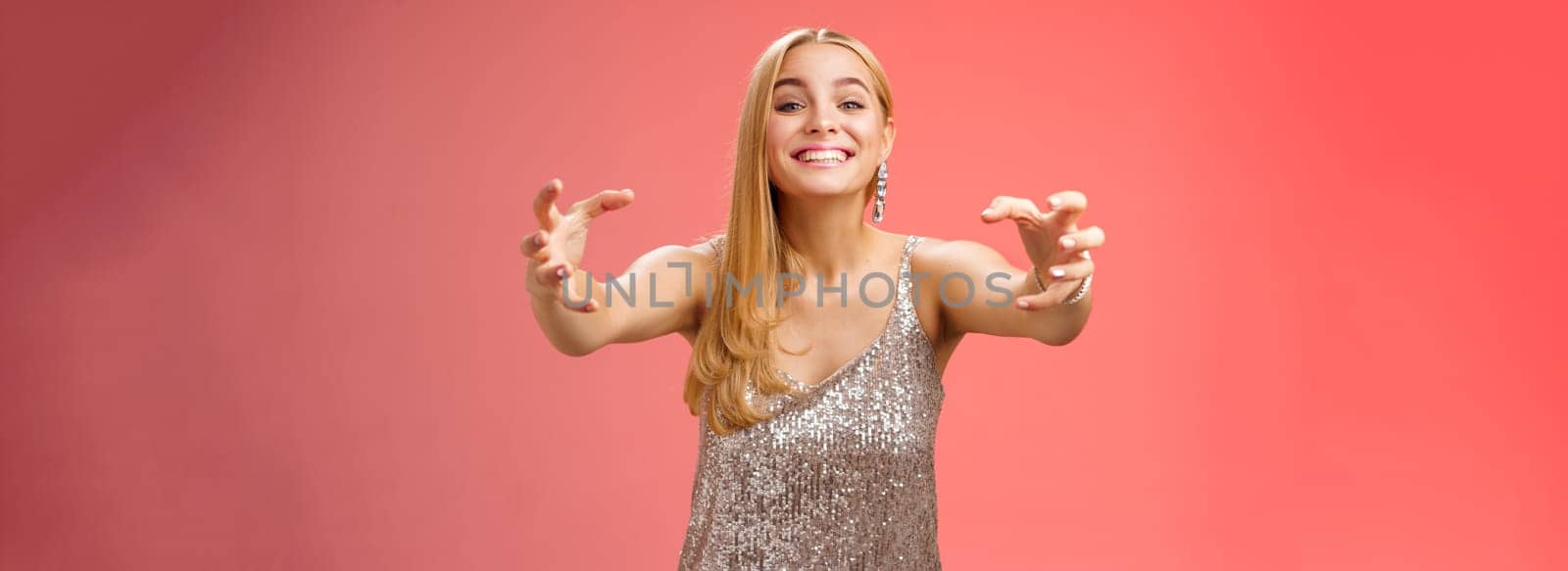 Excited obsessed attractive crazy blond woman in glamour silver dress smiling weird thrilled stretch hands like claws wanna embrace hug ex-boyfriend being clingy, standing red background.