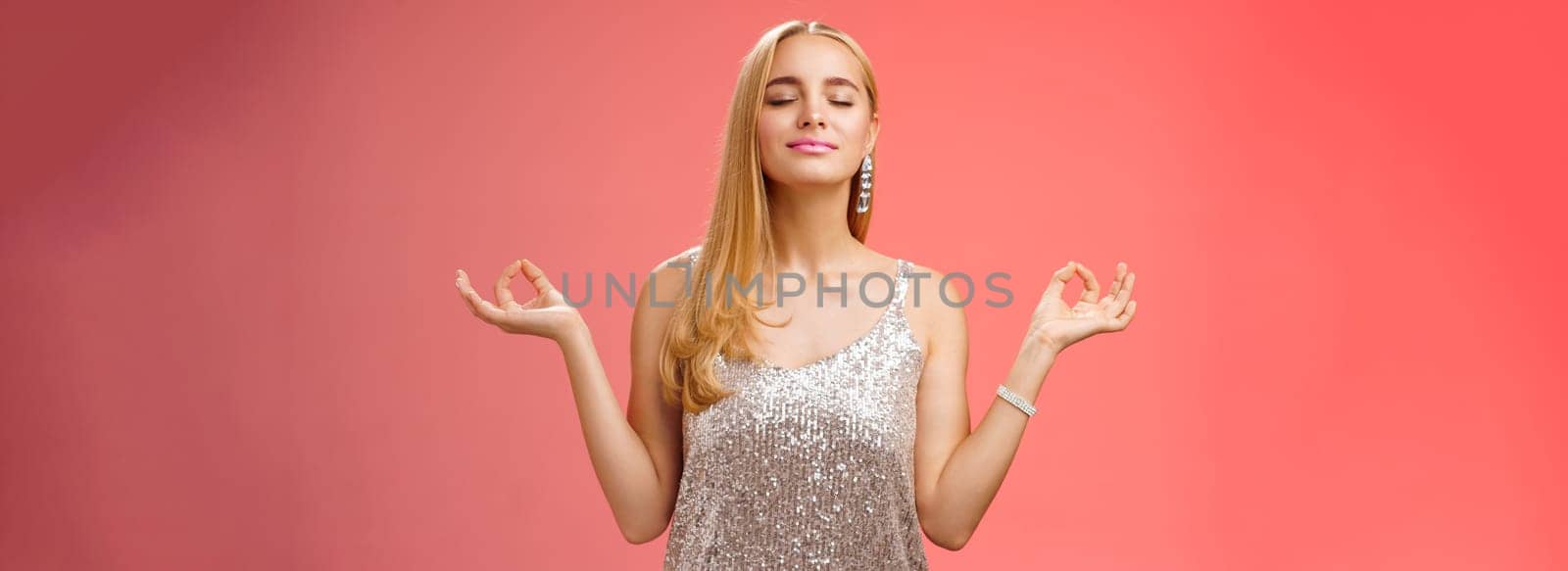 Keep calm party all night. Carefree unbothered happy charming stress-free blond young woman in stylish dress smiling relieved close eyes rejoicing standing lotus nirvana pose, breathing meditating.