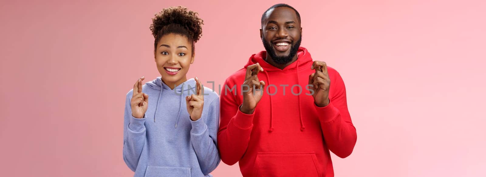 Lucky charming attractive positive african-american friends guy girl cross fingers making wish smiling broadly excited believe faithfully dream come true hopefully look camera, anticipating miracle by Benzoix