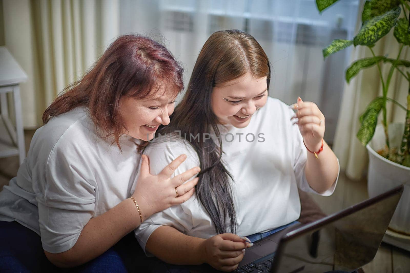 Fat funny funny adult mother and daughter with laptop indoors. A teenage girl teaches a middle-aged woman modern technology. Internet, chatting