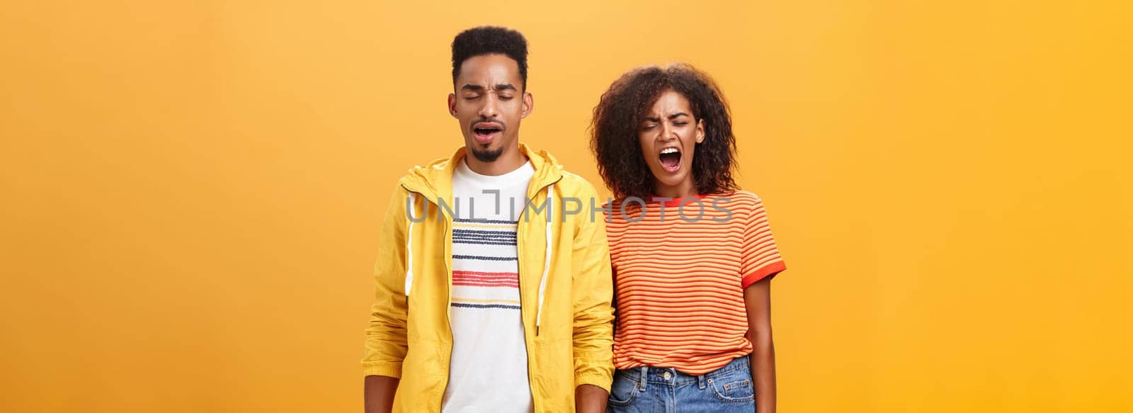 Stylish and attractive brother and sister over orange background yawning with closed eyes and tired expression being drained and exhausted after dealing with house chores cleaning mess after party. Lifestyle.