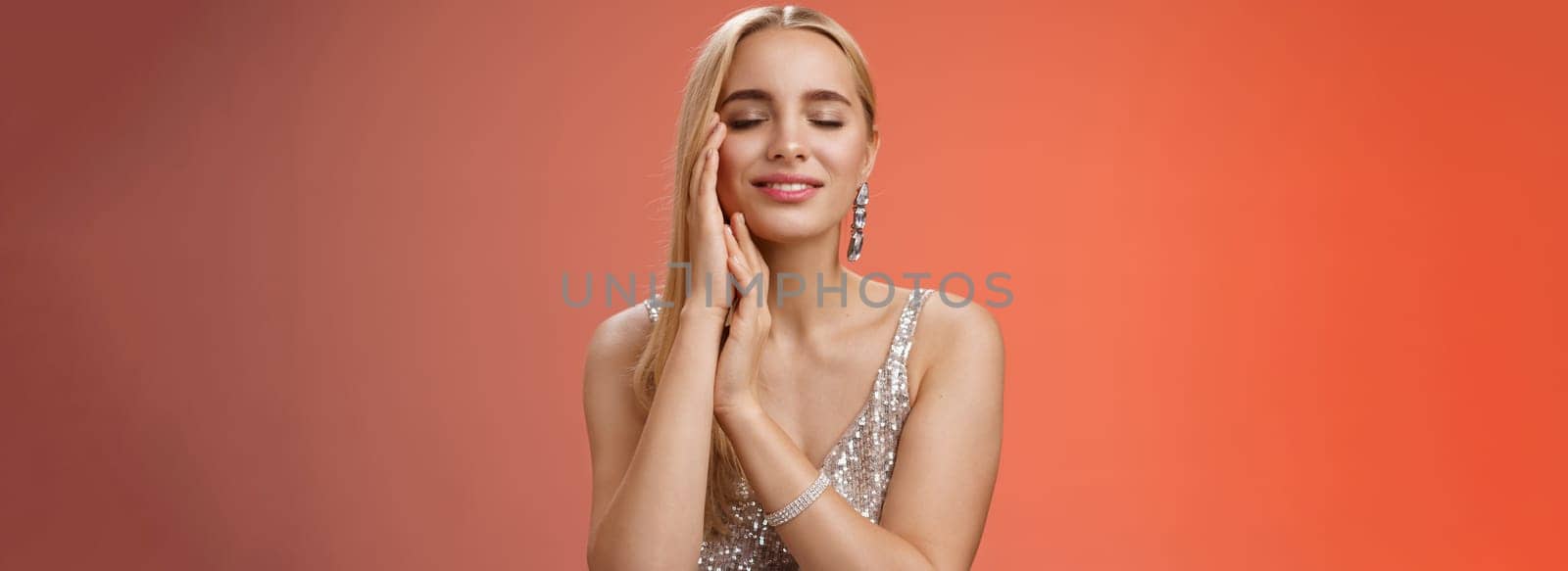 Charming tender lovely coquettish blond woman close eyes smiling relaxed flirty touch face dreaming heartwarming romantic moment, standing red background silver evening dress seducing by Benzoix