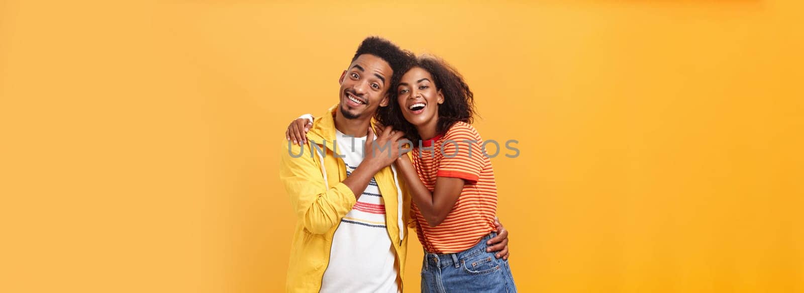 Friends always cover each other. Stylish and carefree loving african american girlfriend hugging boyfriend and smiling broadly touching guy palm hanging around and spending time great together.