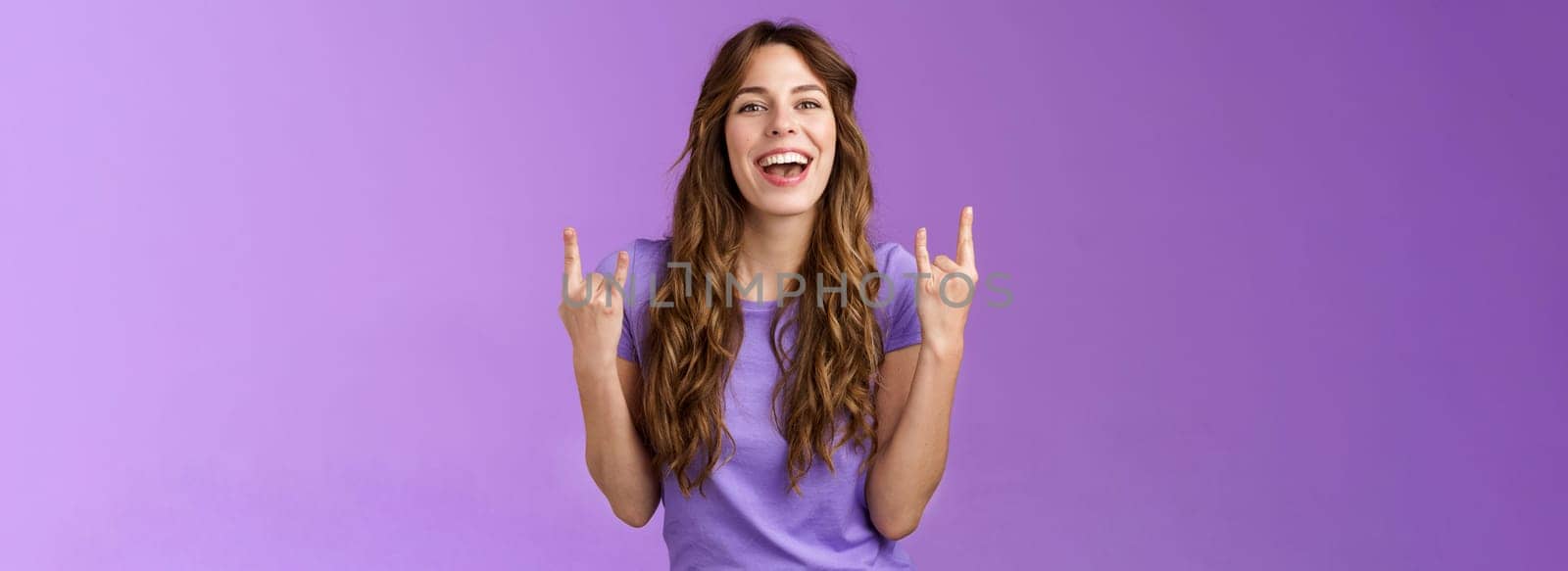 This summer holidays rock. Happy enthusiastic cheerful girl having fun enjoy awesome party weekends smiling broadly say yeah joyful make heavy-metal sign stand purple background amused.