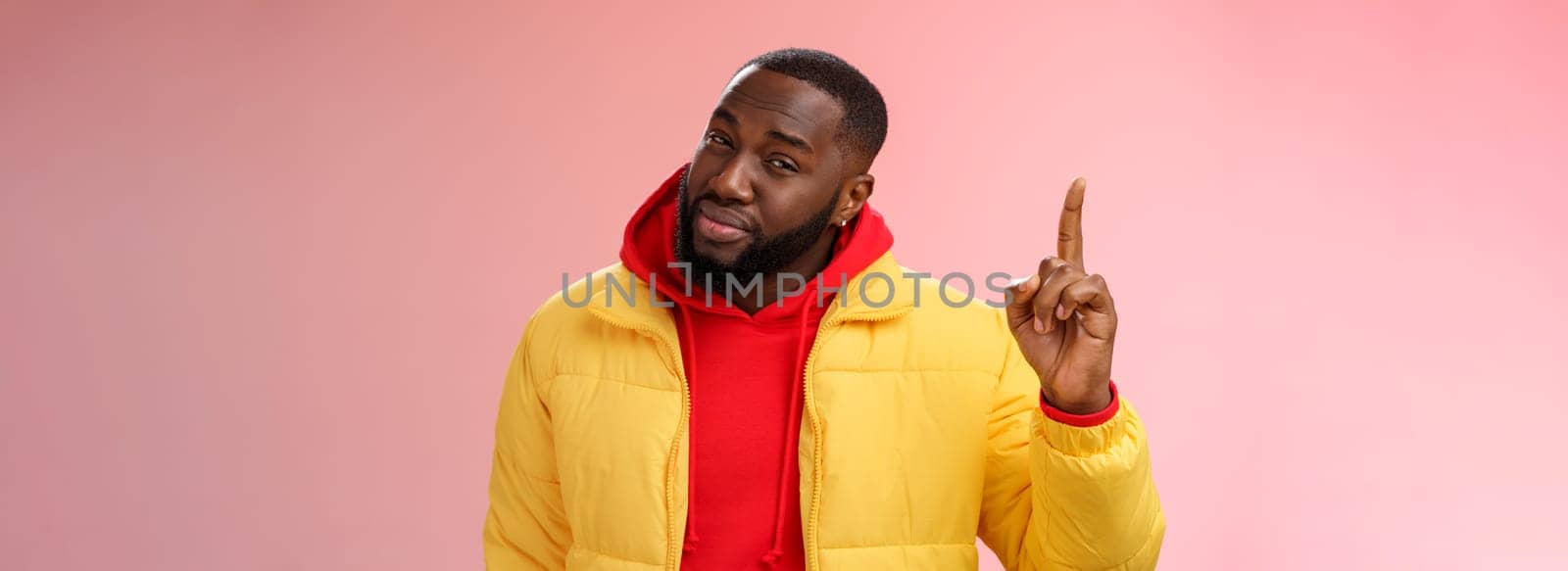 Doubtful displeased african american bearded male customer pointing up index finger squinting cringing disbelief hesitant uncertain product quality, standing questioned frustrated pink background.