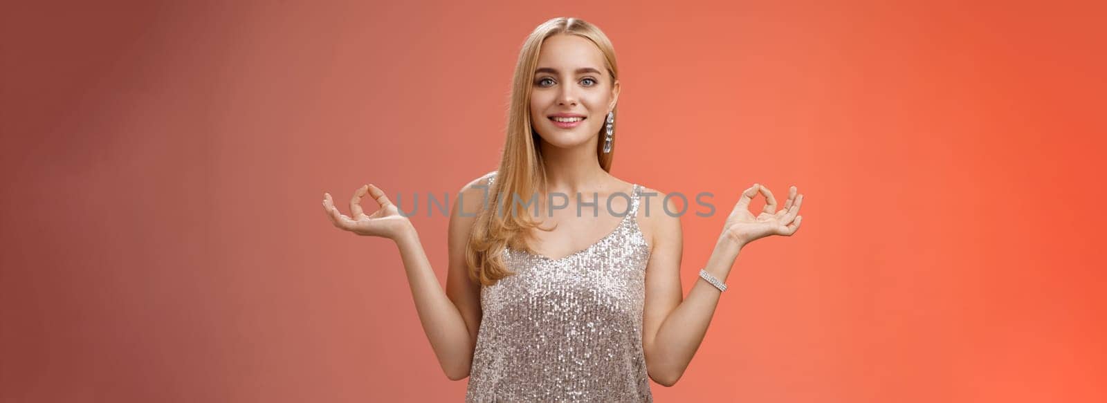 Calm relieved happy fabulous young blond woman in silver stylish luxury dress standing relaxed red background zen lotus pose reach nirvana smiling peaceful carefree meditating breathing practice by Benzoix