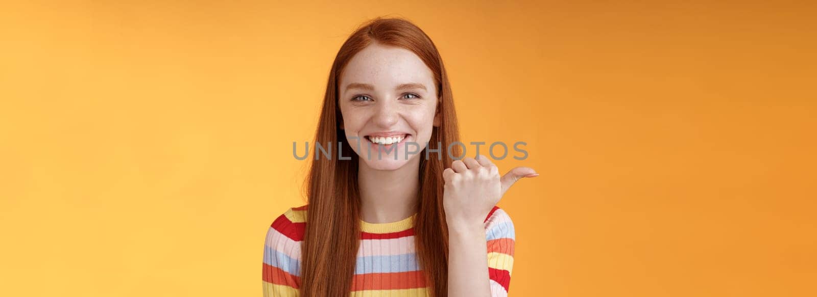 Girl pointing left cool person can help smiling delighted look friendly camera discuss interesting project introduce friend during conversation standing happy grinning orange background.