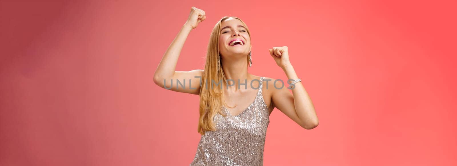 Excited carefree happy stylish blond european woman having fun dancing smiling broadly laughing happiness enjoying awesome music party rocking lighting dance-floor standing red background.