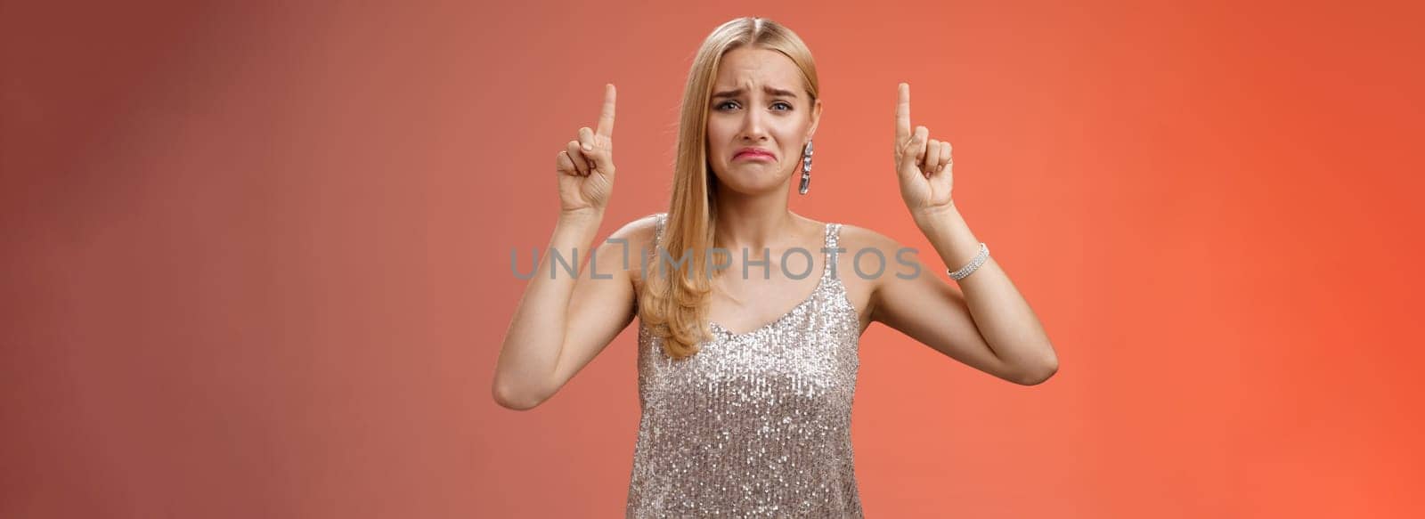 Upset whining immature spoiled blond rich girl in silver glittering dress pouting frowning gonna cry pointing up regret jealousy begging buy expensive shoes, standing red background displeased by Benzoix