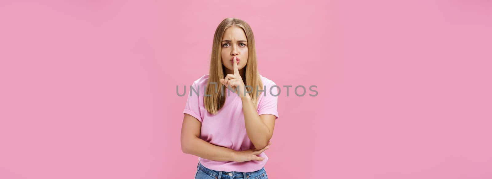 Shh keep voice down. Serious-looking concerned determined female nanny looking after kid asking not speak showing shush gesture with index finger over mouth, having secret concerned someone know it.