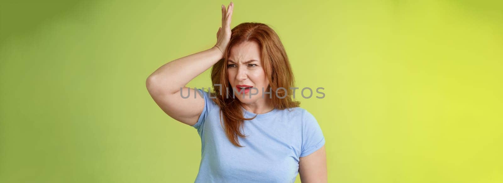Something important slip my mind. Concerned worried upset redhead mature woman punch forehead turn away frustrated frowning disappointed forget cancel appointment stand green background.