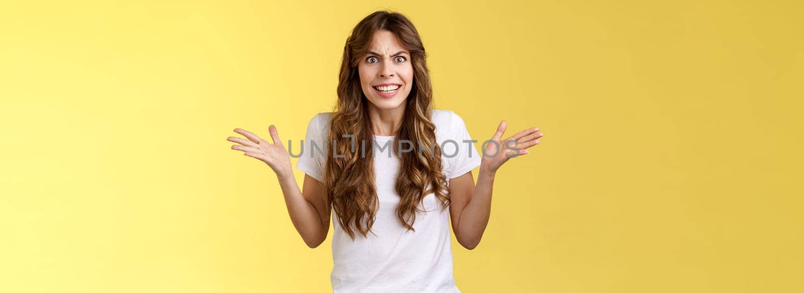 Angry freaked out disappointed woman frowning grimacing anger distress raise hands sideways full dismay complaining being rude arguing look pissed outraged swearing frustrated yellow background.