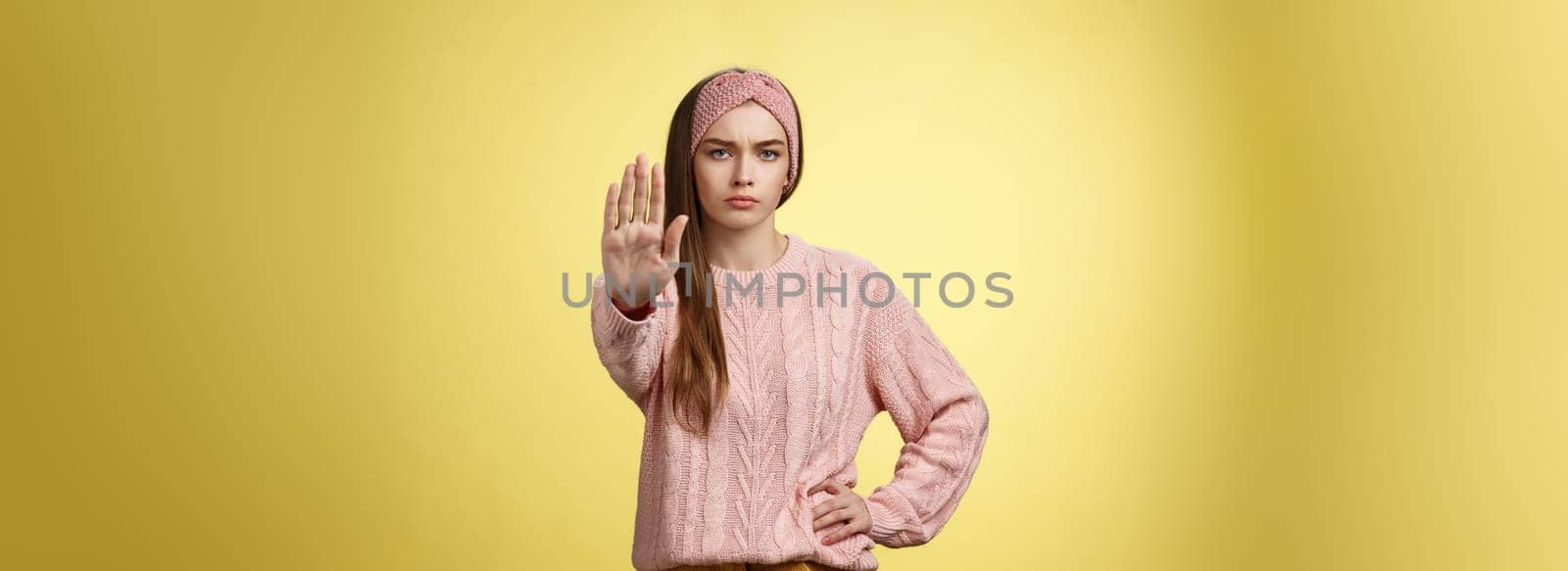 Stop it. Serious-looking confident focused young cute girl extending arm hold, tresspass gesture, frowning displeased, standing bossy denying, forbidding pass, unwilling let-through over yellow wall by Benzoix