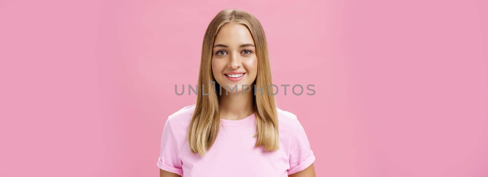 Close-up shot of friendly pleasant commong caucasian girl with fair hair and tanned skin in t-shirt smiling broadly with good white teeth gazing at camera ambitious and delighted over pink background by Benzoix